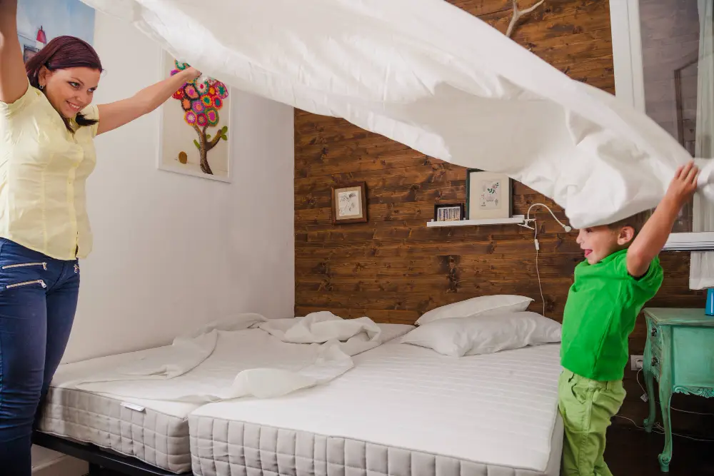 Une mère et son enfant qui soulèvent une couette blanche pour inspecter deux matelas à la recherche de punaises de lit